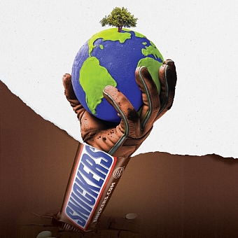 A section of a print ad showing a snickers bar coming up out of a brown background. The advert has been ripped through the middle to reveal a gloved farmer’s hand holding a globe which comes out of the Snickers bar.