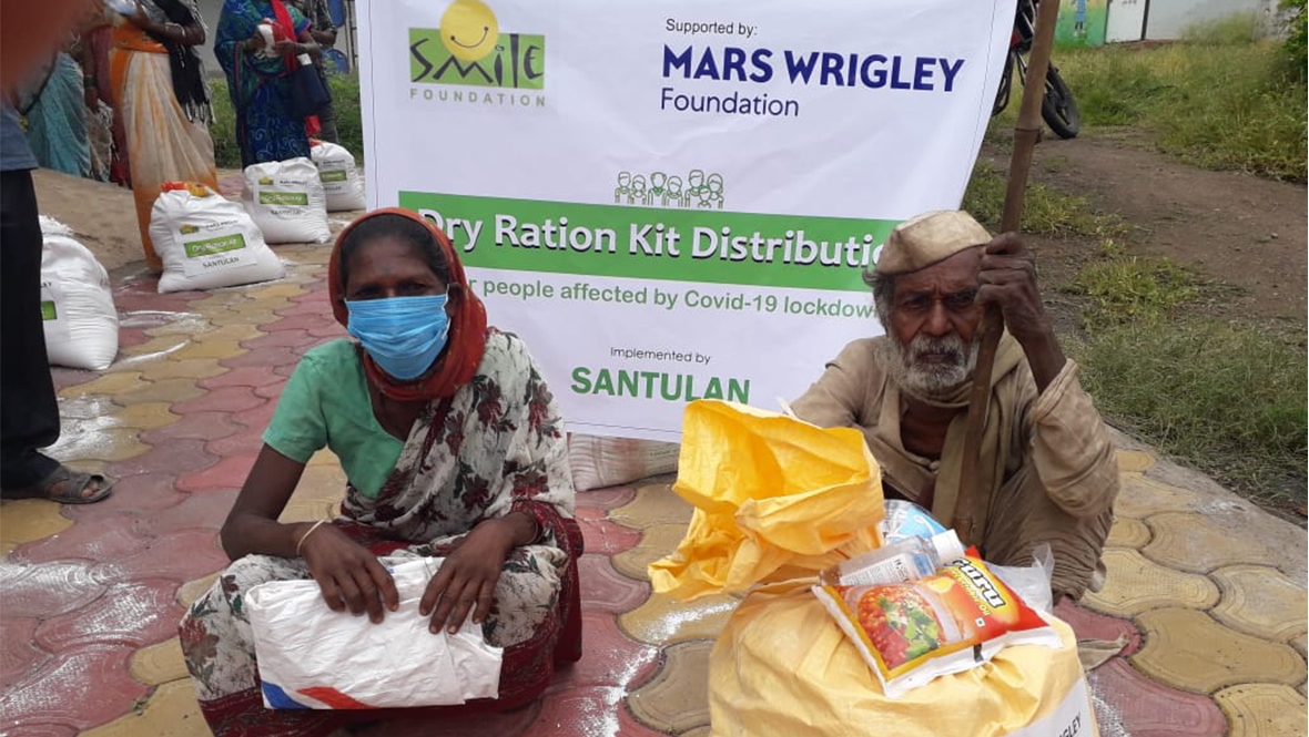 A Mars Wrigley Foundation banner stands behind people beside their large dry-ration kits.