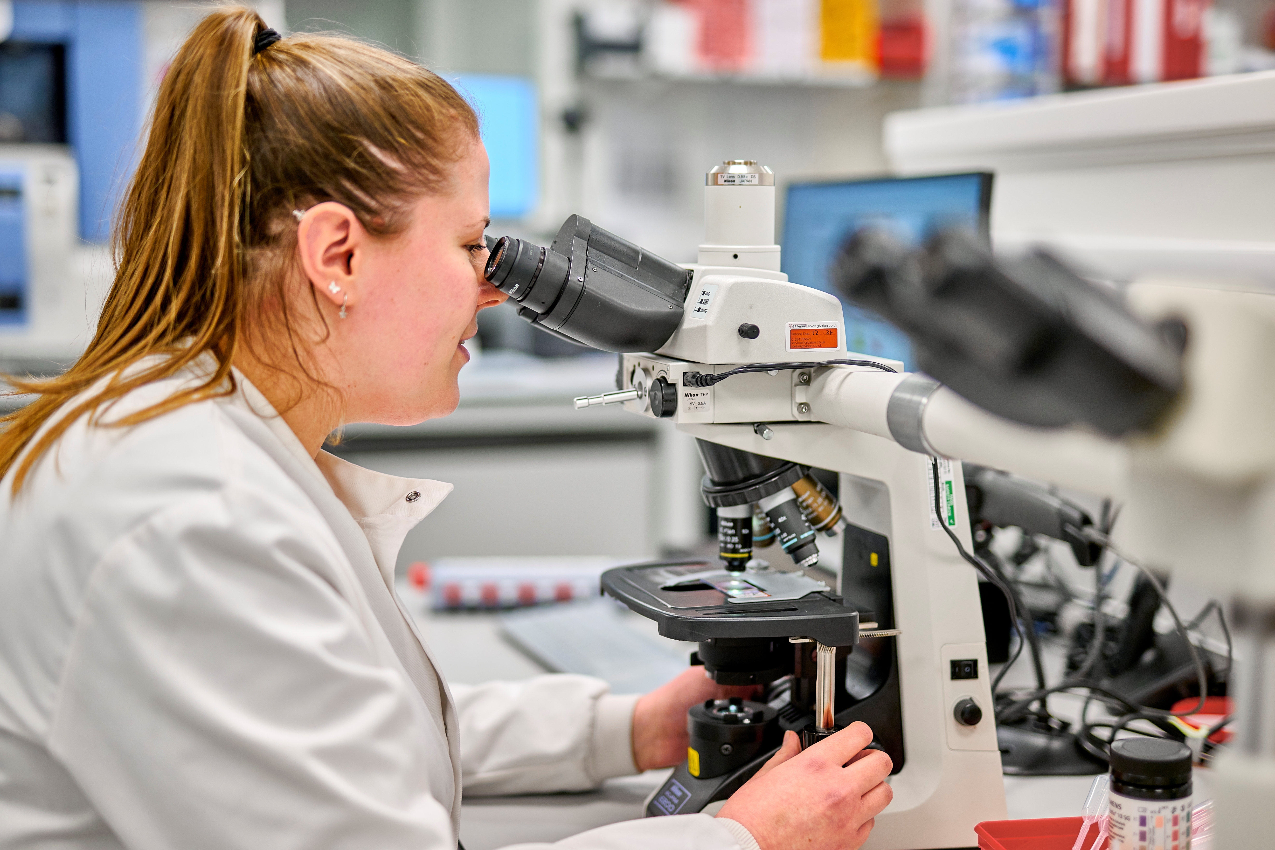 A woman examining a sample under a microscope.