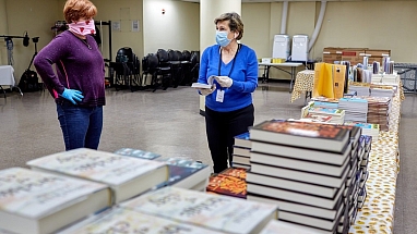 Two Mars Associates from AMERICAN HERITAGE® Chocolate wearing masks beside donated books.