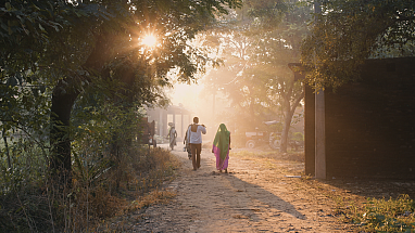 Man and woman walking on a dirt road as the sun sets.