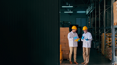 Two men wearing hard hats and talking in a warehouse