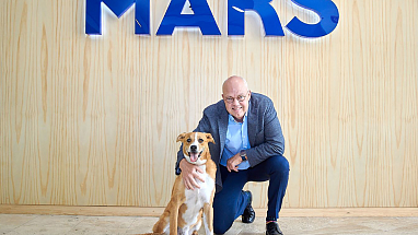 Poul Weihrauch kneeling with a dog, in front of the Mars logo