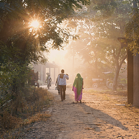 Man and woman walking on a dirt road as the sun sets.