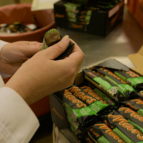 Person holding a Mars bar, in front of a box of Mars bars with new recyclable paper packaging