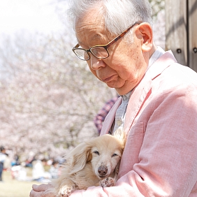 An older man in a pink coat, holding a blonde Daschund