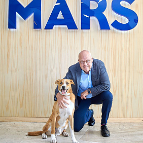 Poul Weihrauch kneeling with a dog, in front of the Mars logo