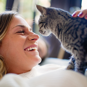 A woman smiling while petting a kitten