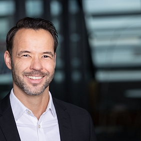 ein lächelnder Mann in einem dunklen Anzug und weißem Hemd