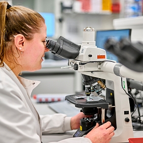 A woman examining a sample under a microscope.
