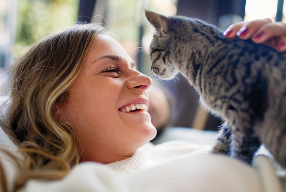 A woman smiling while petting a kitten